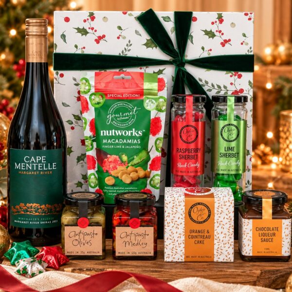 Festive Celebration Christmas hamper featuring Cape Mentelle Shiraz, gourmet savoury treats, sherbet sweets and chocolate stars beside a holly-patterned gift box with green velvet ribbon.
