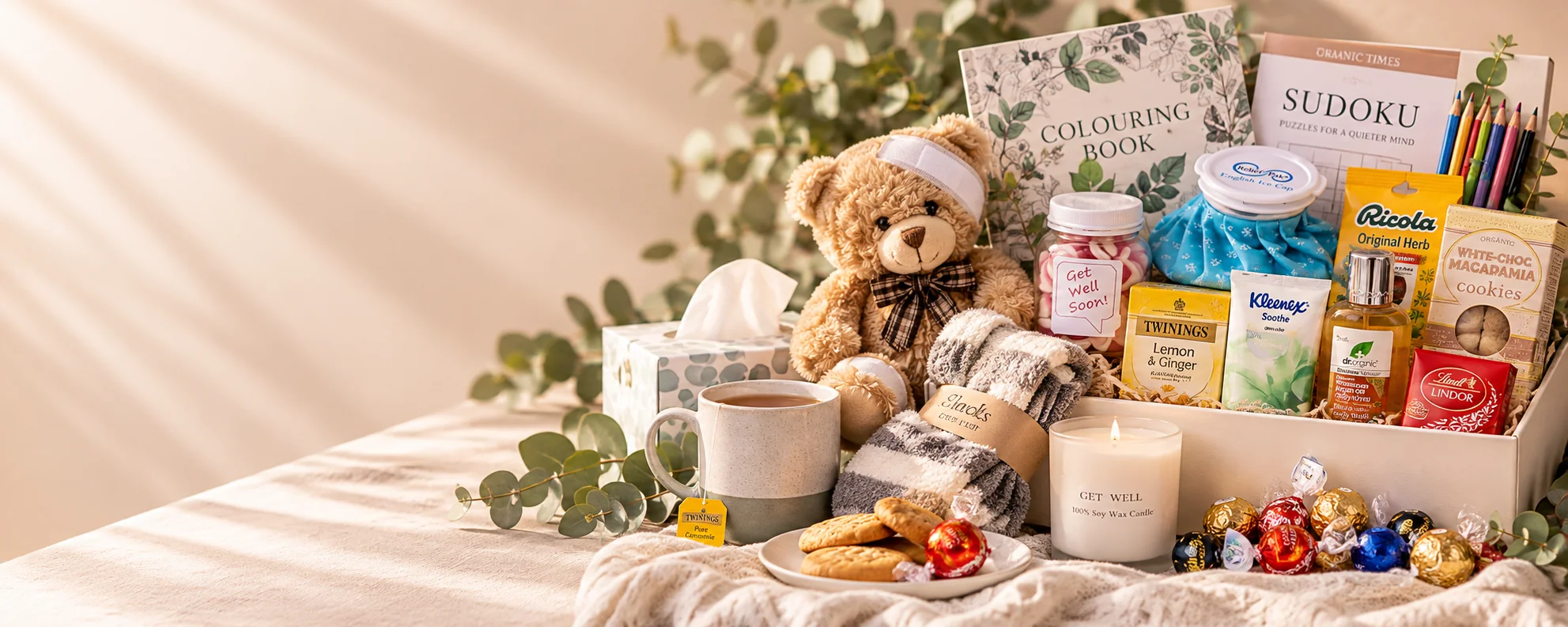 Get well gift setting with a teddy bear, colouring and puzzle books, tea, cosy socks, candle, treats and comfort items
